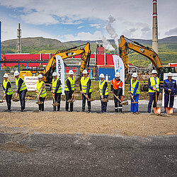 Photo: Aurubis: Many people wearing helmets and neon vests stand in a row on a construction site, each with a shovel in their hand