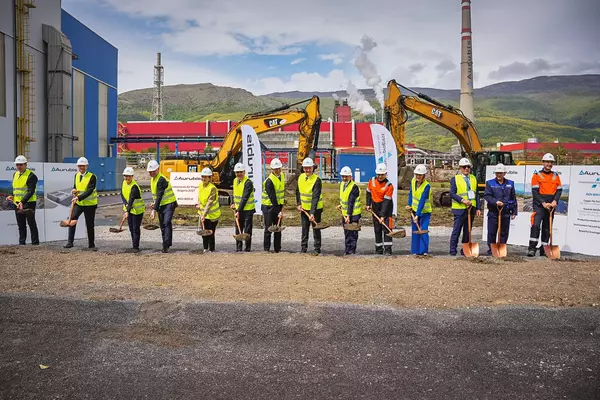 Photo: Aurubis: Many people wearing helmets and neon vests stand in a row on a construction site, each with a shovel in their hand