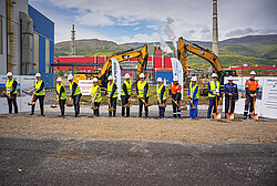 Photo: Aurubis: Many people wearing helmets and neon vests stand in a row on a construction site, each with a shovel in their hand
