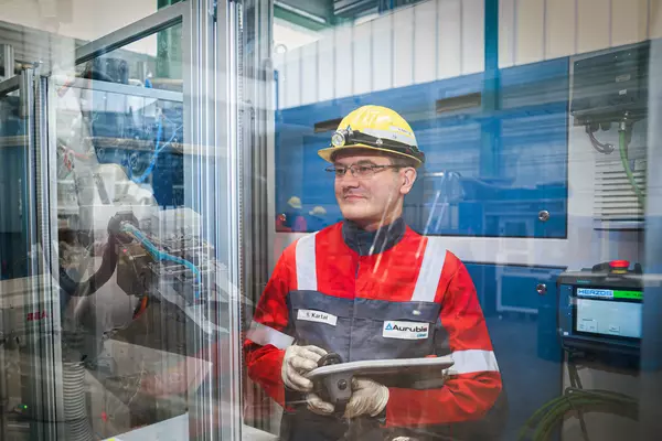 Photo: Aurubis: A man in a yellow helmet and Aurubis jacket stands in front of a glass wall and holds a device in his hand