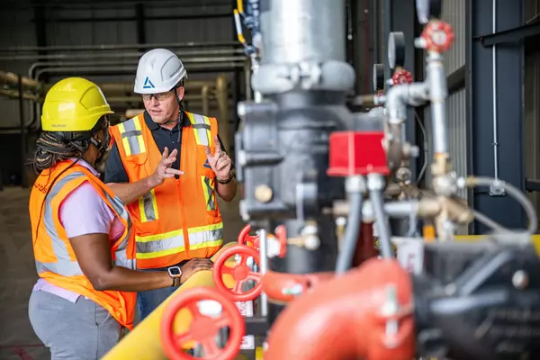 Photo: Aurubis: Three workers in safety clothing talking to each other in front of a large industrial machine