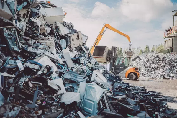 Photo: Aurubis: A yellow excavator sorts a large pile of scrap at a scrap yard