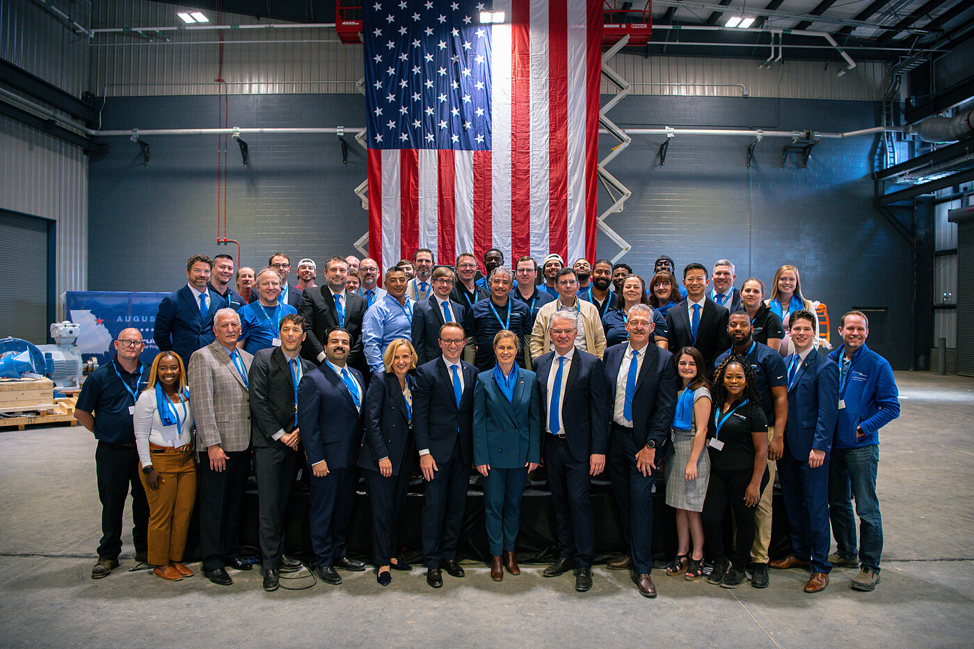 Photo: Aurubis: Group photo of formally dressed people in a hall, behind them is a large USA flag