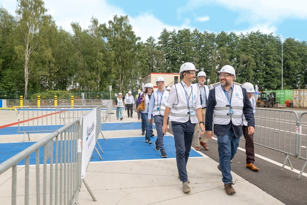 Photo: Aurubis: Several people wearing helmets and vests, walking along a road between metal fences