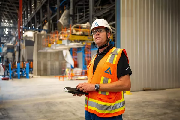 Foto: Aurubis: Ein Mann in einer Sicherheitsweste und einem Helm hält ein Geraet in der Hand und steht auf einer Baustelle