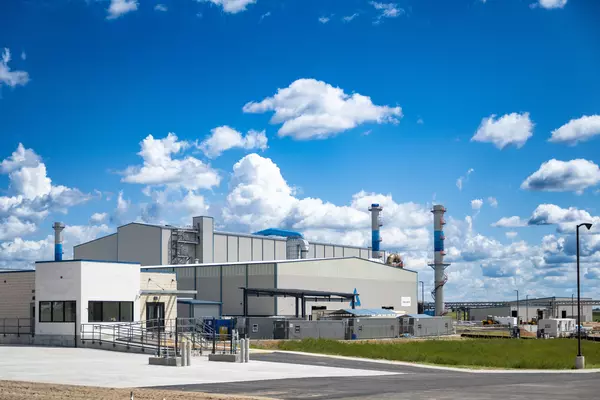 Foto: Aurubis: Industrieanlage mit hellen Gebäuden unter einem blauen Himmel mit weissen Wolken